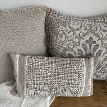 Kissenhülle Jacquard 3D Waffelmuster in Taupe-Beige, dekorativ arrangiert mit weiteren Kissen in neutralen Tönen auf einer Holzbank.